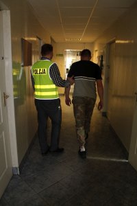 policjant w kamizelce z napisem POLICJA prowadzi zatrzymanego.