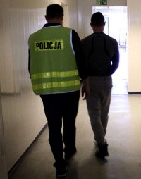 nieumundurowany policjant w kamizelce z napisem POLICJA prowadzi zatrzymanego.