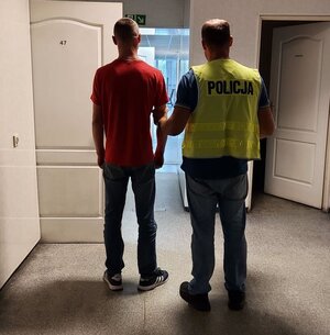 policjant w kamizelce z napisem POLICJA prowadzi zatrzymanego.