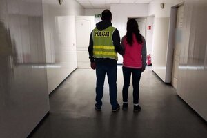 policjant w kamizelce z napisem POLICJA prowadzi zatrzymaną kobietę.