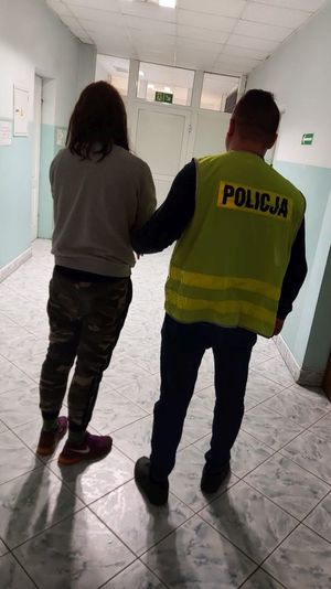 nieumudurowany policjant w kamizelce z napisem Policja prowadzi osobę zatrzymaną.