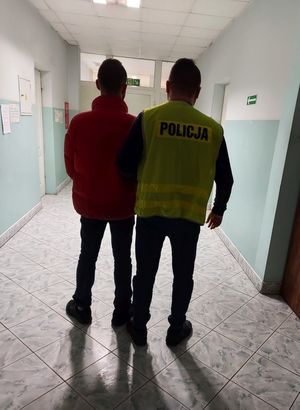 nieumundurowany policjant w kamizelce z napisem Policja prowadzi osobę zatrzymaną.