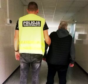 nieumundurowany policjant w kamizelce z napisem POLICJA Technik Kryminalistyki prowadzi zatrzymanego.