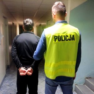 nieumundurowany policjant w kamizelce z napisem POLICJA prowadzi zatrzymanego.