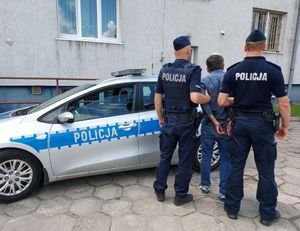 umundurowani policjanci prowadzą zatrzymanego, w tle widać radiowóz.