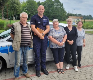 Dzielnicowy z grupą seniorów na tle radiowozu.