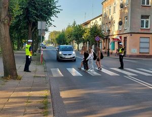 policjanci pomagają przejść na drugą stronę jezdni dzieci.