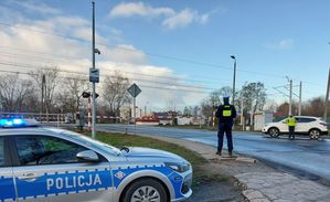 policjanci w rejonie przejazdu kolejowego wręczają kierowcom ulotki, w tle radiowóz.