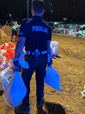 policjanci pomagają przy napełnianiu worków z piaskiem.