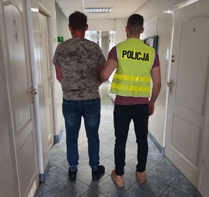 policjant w kamizelce z napisem POLICJA prowadzi zatrzymanego.