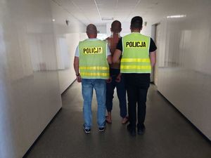 policjanci w kamizelkach z napisem POLICJA prowadzą zatrzymanego.