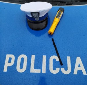 Czapka funkcjonariusza wydziału ruchu drogowego, alkomat na tle napisu Policja.