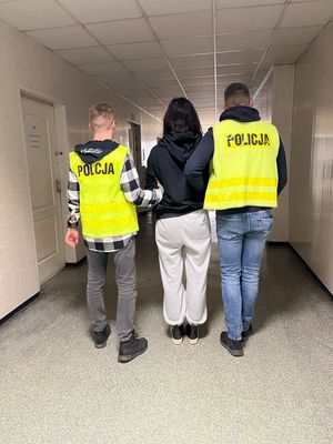 dwóch policjantów stojących tyłem z zatrzymaną.