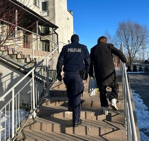 policjant odprowadza osobę zagrożoną wychłodzeniem do placówki dla osób w kryzysie.