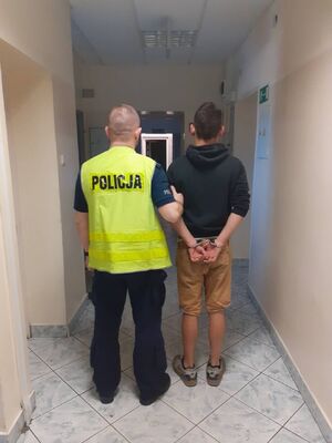 policjant w kamizelce z napisem POLICJA prowadzi zatrzymanego.