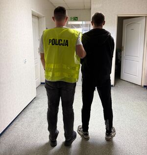 policjant w kamizelce z napisem policja prowadzi zatrzymanego.