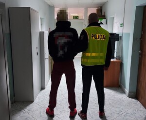 policjant w kamizelce z napisem POLICJA prowadzi zatrzymanego.