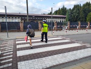 policjantka prowadzi dziecko po przejściu dla pieszych.