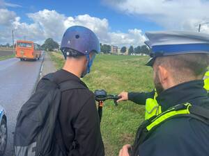 policjant ruchu drogowego kontroluje osobę na hulajnodze elektrycznej i przekazuje kask.