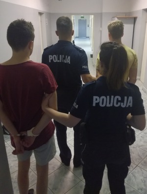 na zdjęciu dwóch zatrzymanych .Przy każdym z nich umundurowany policjant ( funkcjonariusz i funkcjonariuszka)